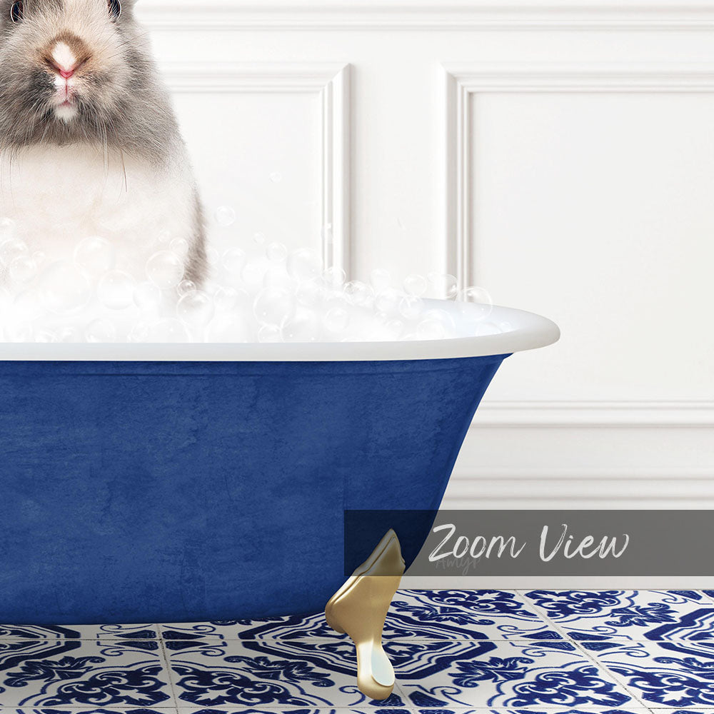 A fluffy gray and white rabbit sitting in a blue bathtub filled with bubbles, with a white wall and a patterned tile floor in the background.