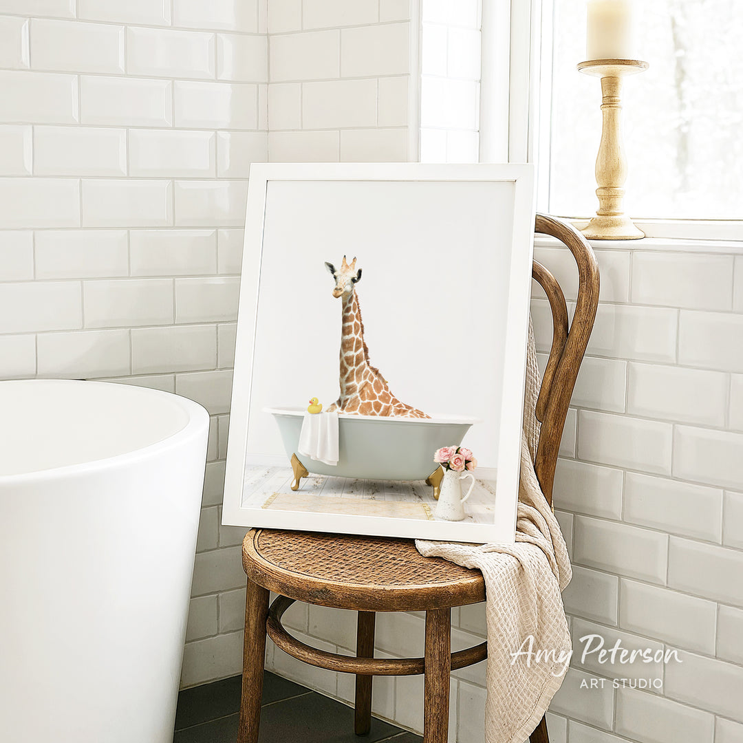 A framed image of a giraffe sitting in a bathtub, surrounded by flowers, is displayed on a wooden chair in a bathroom setting.