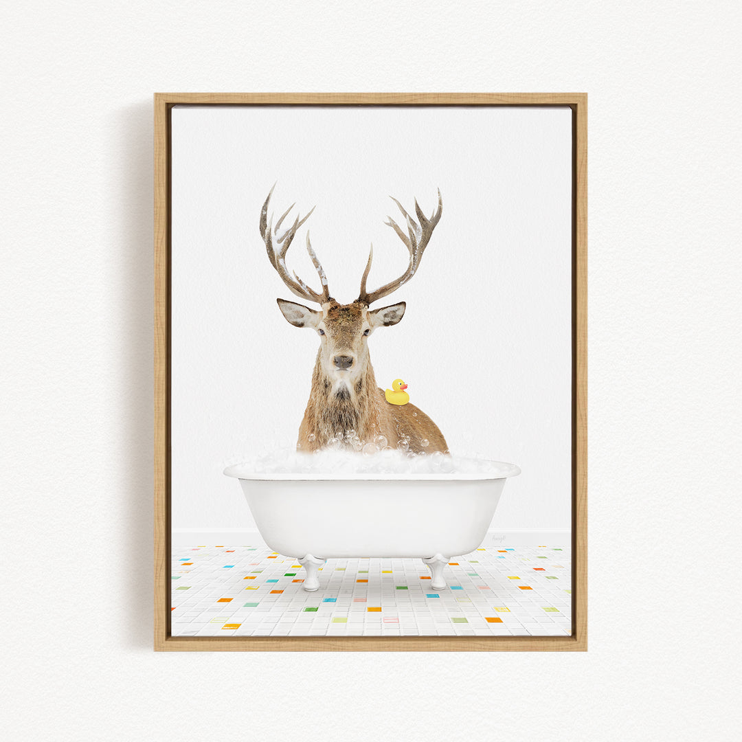 A deer with large antlers is sitting in a white bathtub filled with bubbles, with a yellow rubber duck perched on its head.
