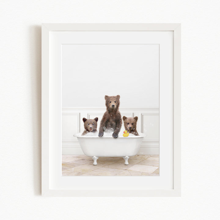 A framed image showing three brown bears sitting in a white bathtub, with one bear holding a yellow rubber duck.