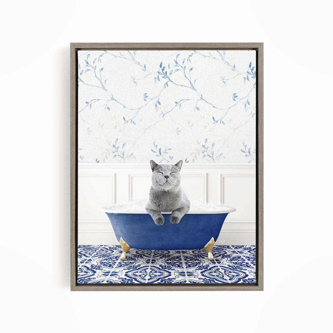 A gray cat sitting in a blue bathtub filled with bubbles, with a patterned tile floor and a floral wallpaper in the background.