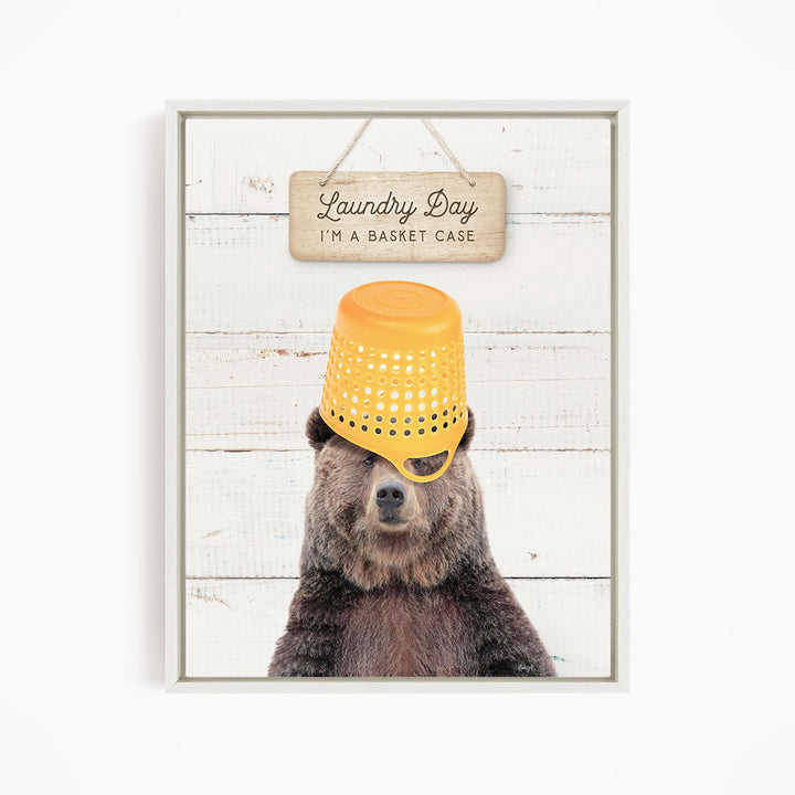 A framed image of a bear wearing a yellow plastic basket on its head, with a sign above that says "Laundry Day I'm a basket case".