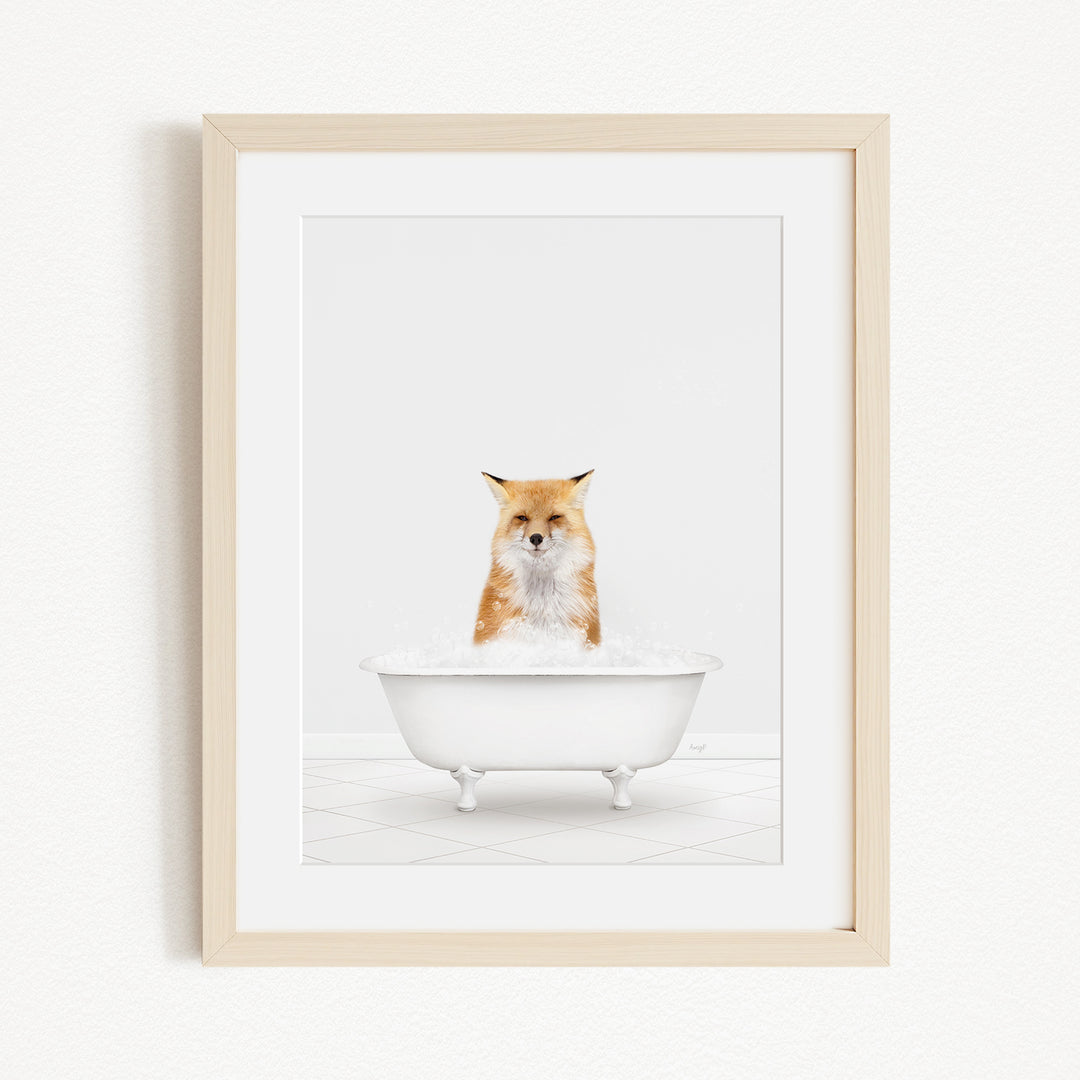 A red fox is sitting in a white bathtub filled with bubbles, looking directly at the camera.