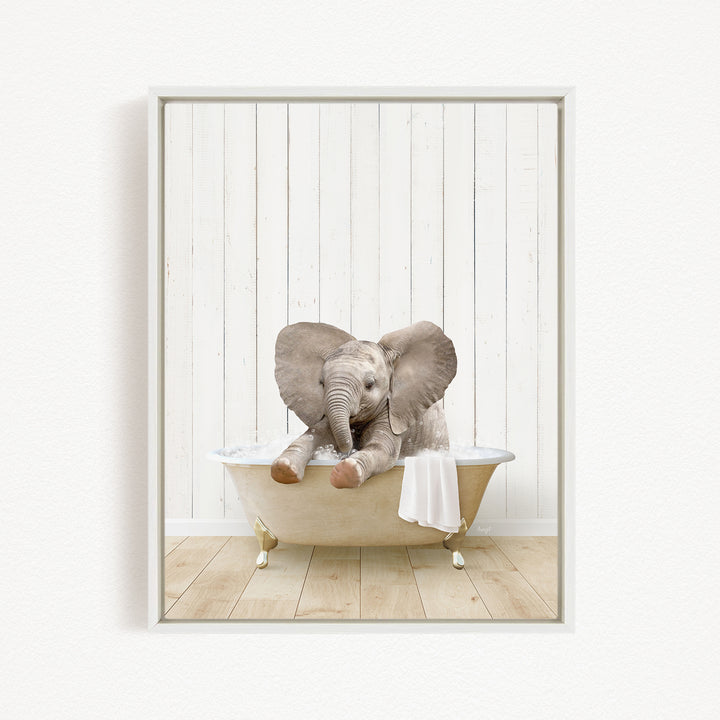A baby elephant sitting in a bathtub, with its trunk in its mouth, against a white wooden wall.