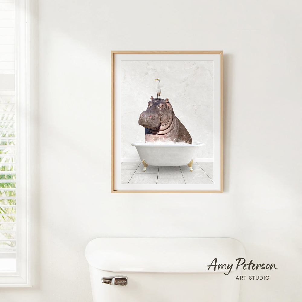 A framed image of a hippopotamus sitting in a bathtub is hanging on a white wall.