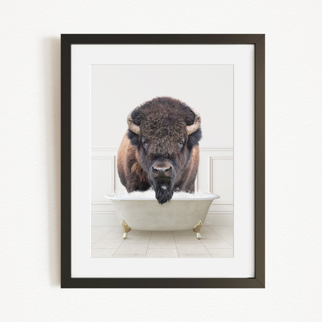 A buffalo with a black mane and horns is sitting in a white bathtub, with its head in the water.