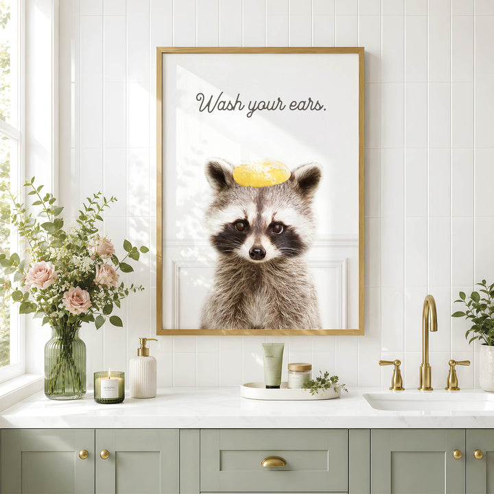 a bathroom with a framed picture of a raccoon wearing a yellow hat, a sink, a vase with flowers, and a framed quote about washing ears.
