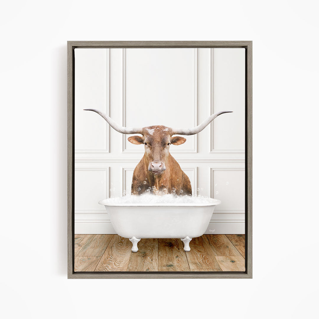 A brown steer with large horns is sitting in a white bathtub, surrounded by bubbles, in a white-walled room.