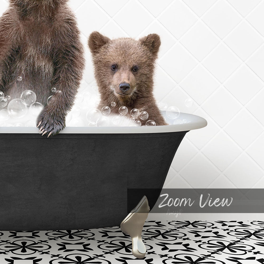 A young bear cub sitting in a bathtub filled with bubbles, with a black bathtub and a patterned tile floor visible in the image.