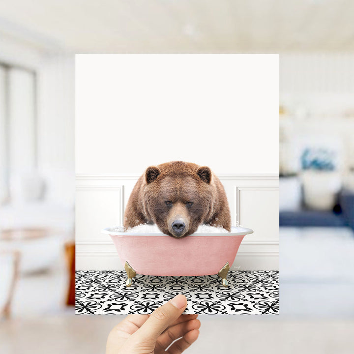 A brown bear sitting in a pink bathtub filled with water, with a hand holding the image up to the camera.