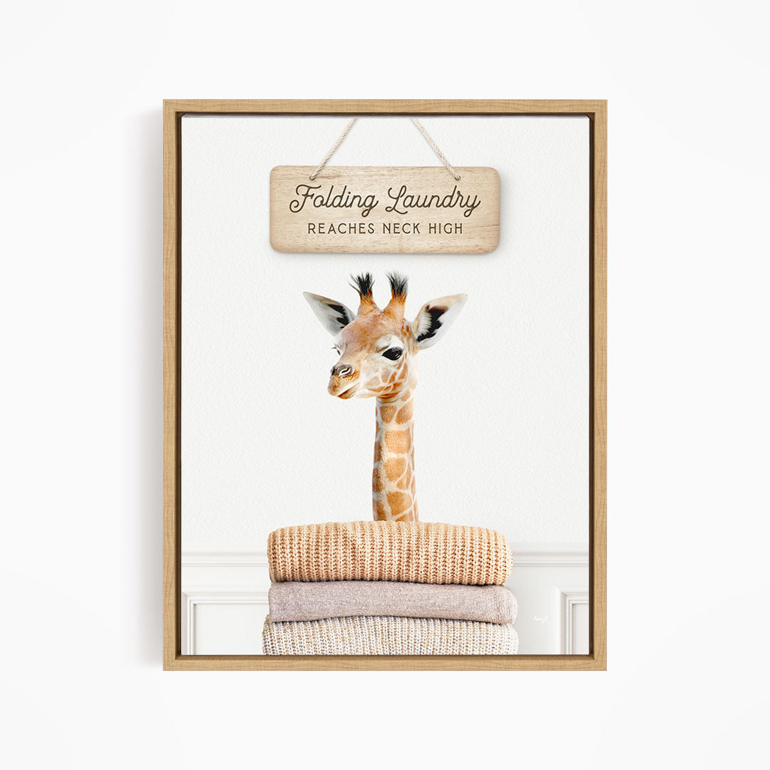 A giraffe standing on a pile of folded clothes, with a wooden sign above that says "Folding Laundry Reaches Neck High".