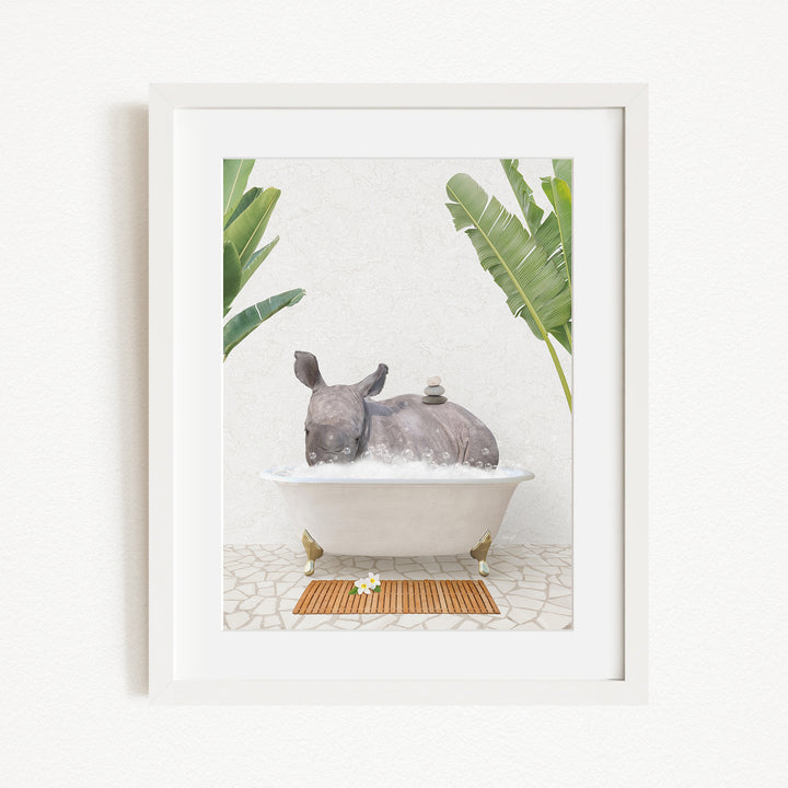 A framed image depicting a rhinoceros sitting in a bathtub filled with water, surrounded by tropical plants.