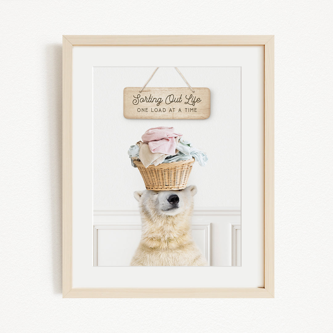 A polar bear balancing a basket of laundry on its head, with a wooden sign above that reads "Sorting Out Life One Load at a Time".
