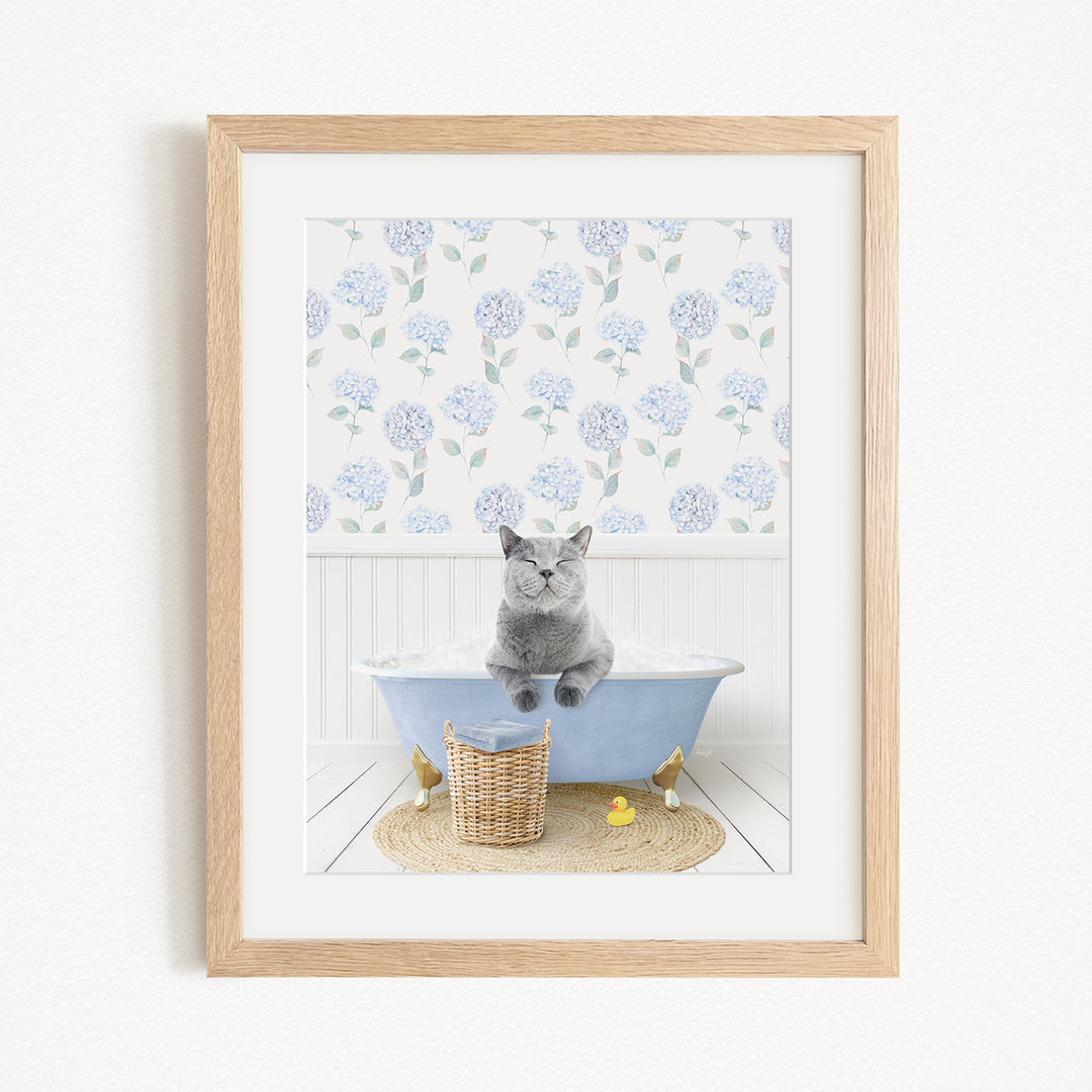 A gray cat sitting on a blue bathtub, surrounded by a floral patterned wall, a basket, and a yellow rubber duck.