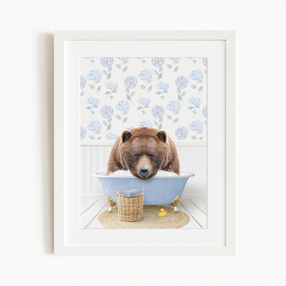 A brown bear is sitting in a blue bathtub filled with water, surrounded by a floral patterned wall and a basket of rubber ducks.