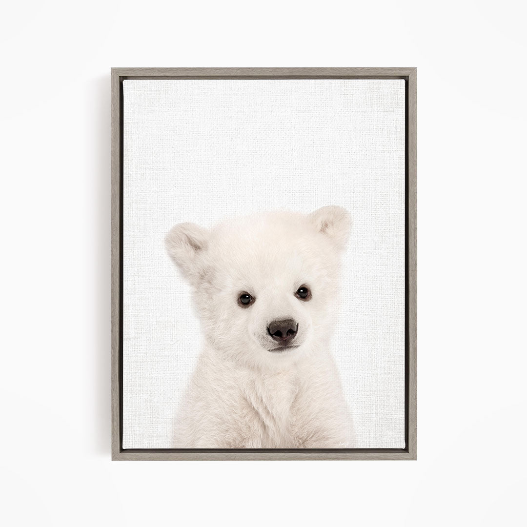A cute white polar bear cub with large eyes and a black nose is the focus of the image.