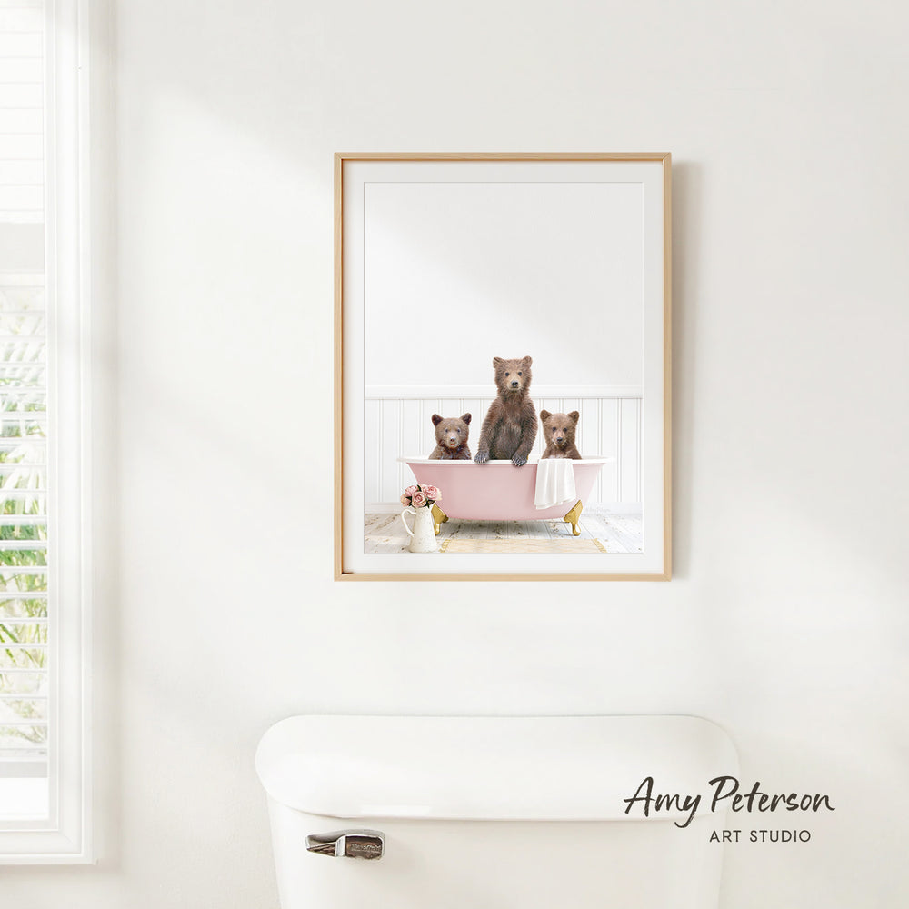 A framed image of three bears sitting in a pink bathtub, with a window and a toilet visible in the background.