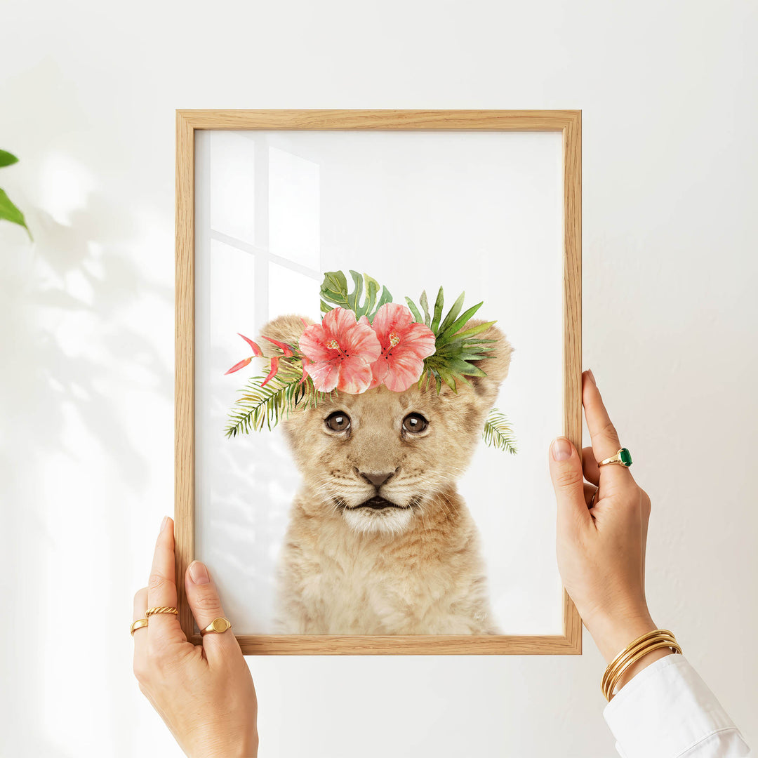 A person's hands are holding a picture frame with a young lion wearing a floral crown.