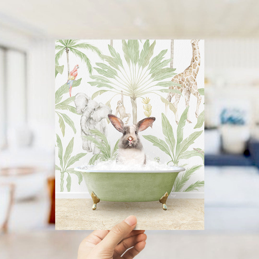 A hand holds up a framed print featuring a whimsical illustration of a rabbit sitting in a bathtub surrounded by tropical foliage, including a giraffe and other animals.