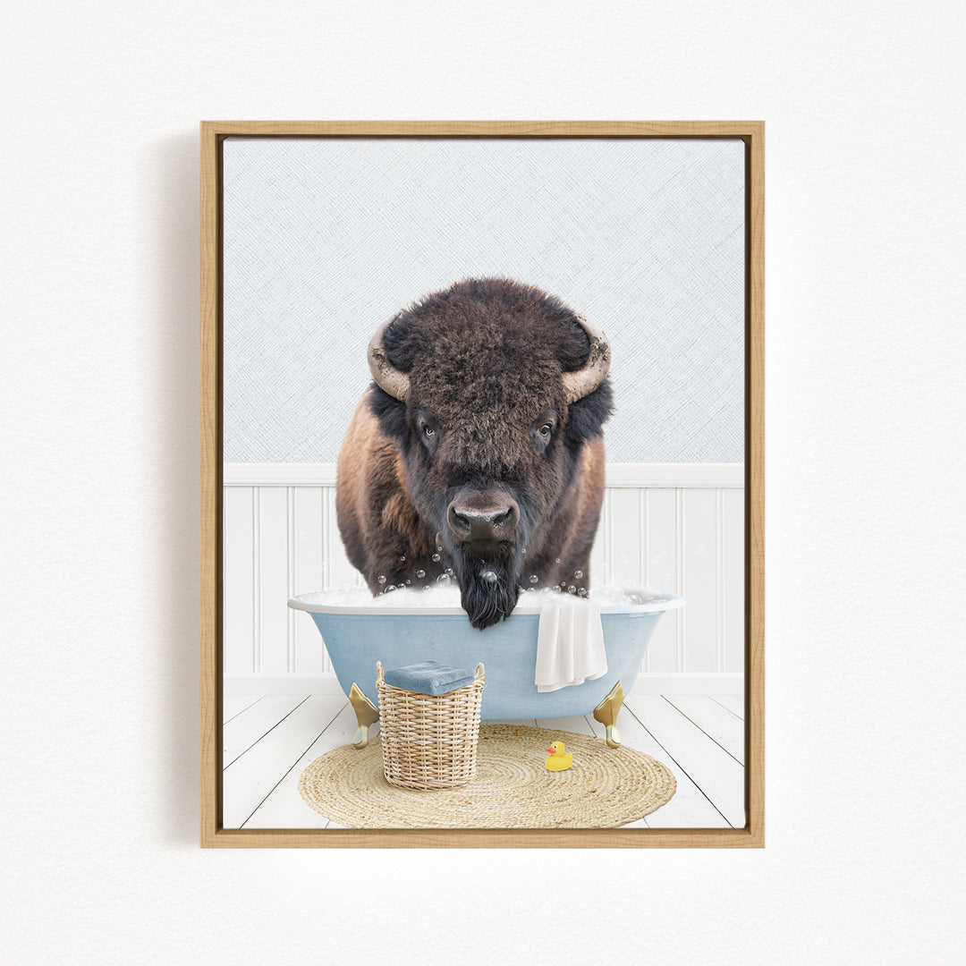 A buffalo with large horns is sitting in a blue bathtub filled with water, surrounded by a basket, a yellow rubber duck, and a towel.