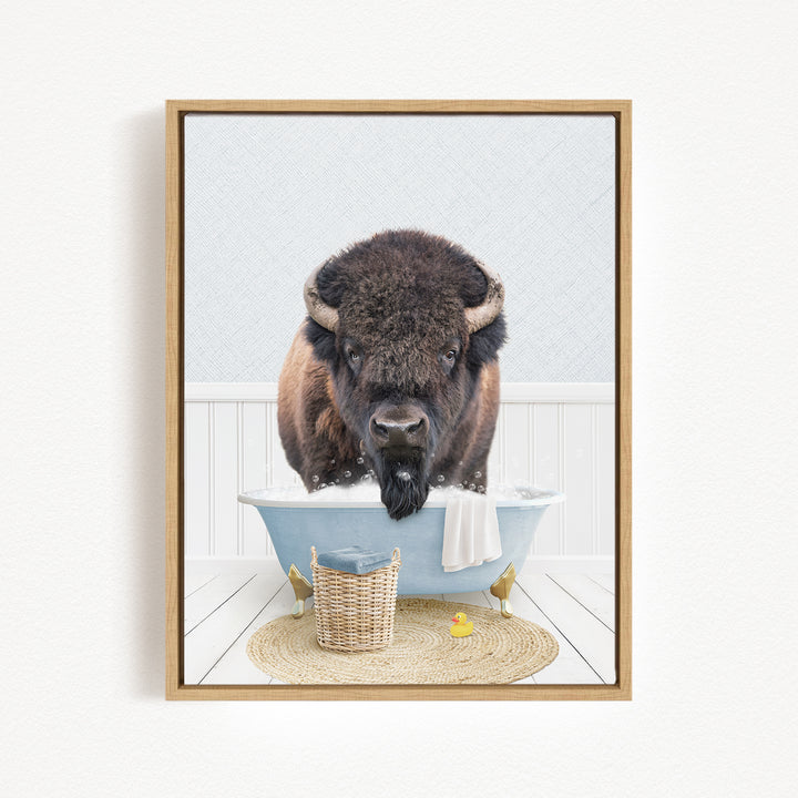 A buffalo with large horns is sitting in a blue bathtub filled with water, surrounded by a basket, a yellow rubber duck, and a towel.