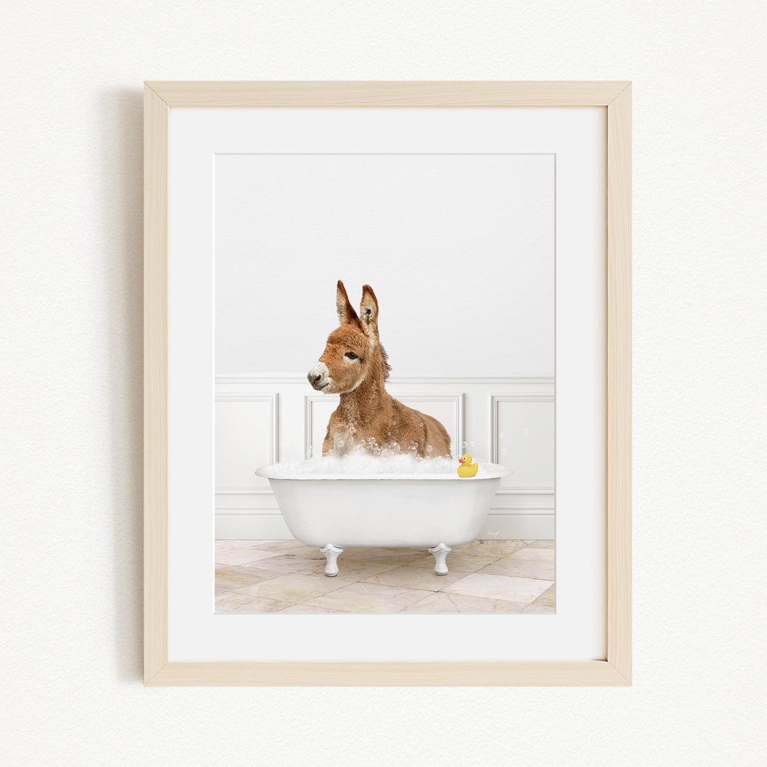 A donkey is sitting in a white bathtub filled with bubbles, with a yellow rubber duck floating in the water.