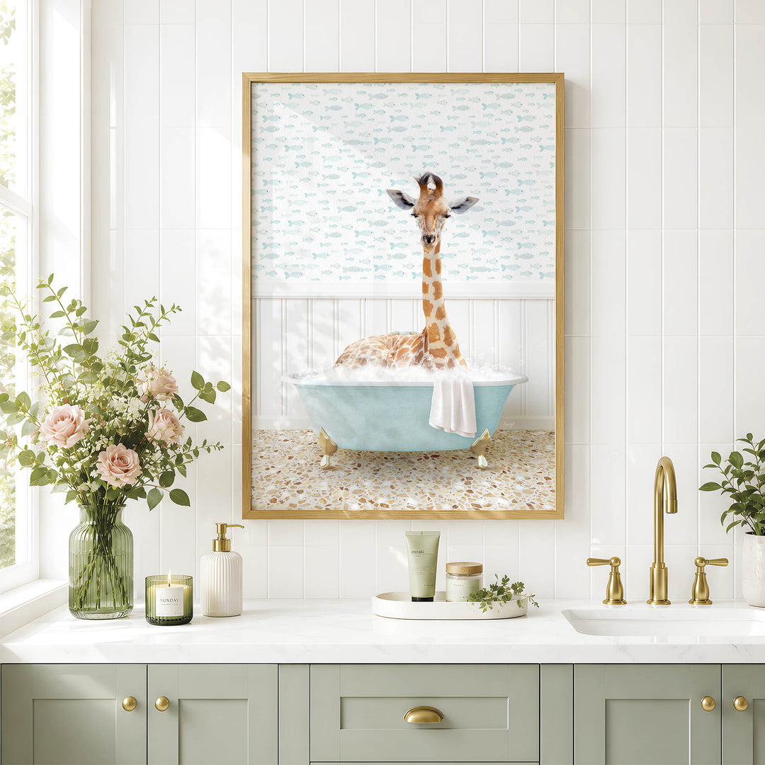 A giraffe sitting in a blue bathtub, surrounded by flowers and a framed picture, in a bathroom setting with a white countertop and gold fixtures.