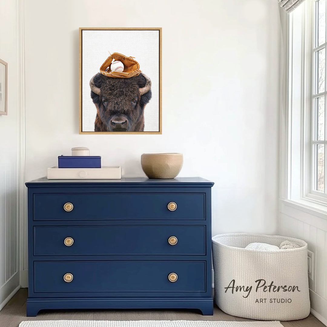 a blue dresser with a framed picture of a buffalo resting its head on a baseball glove on top of it. The dresser is situated in a room with white walls and a window.