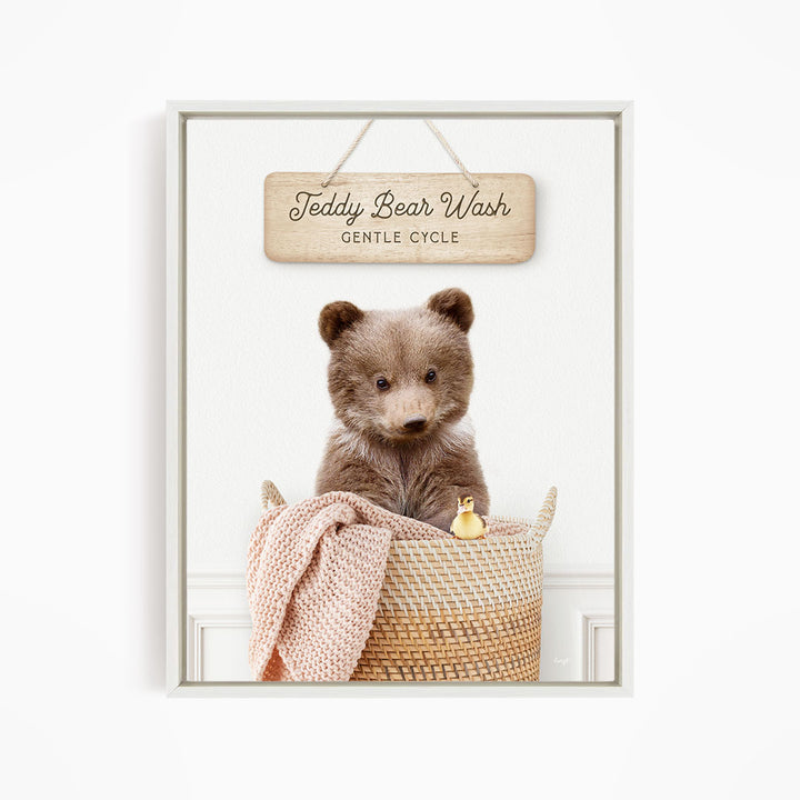 A teddy bear sitting in a woven basket, with a sign above that reads "Teddy Bear Wash Gentle Cycle".