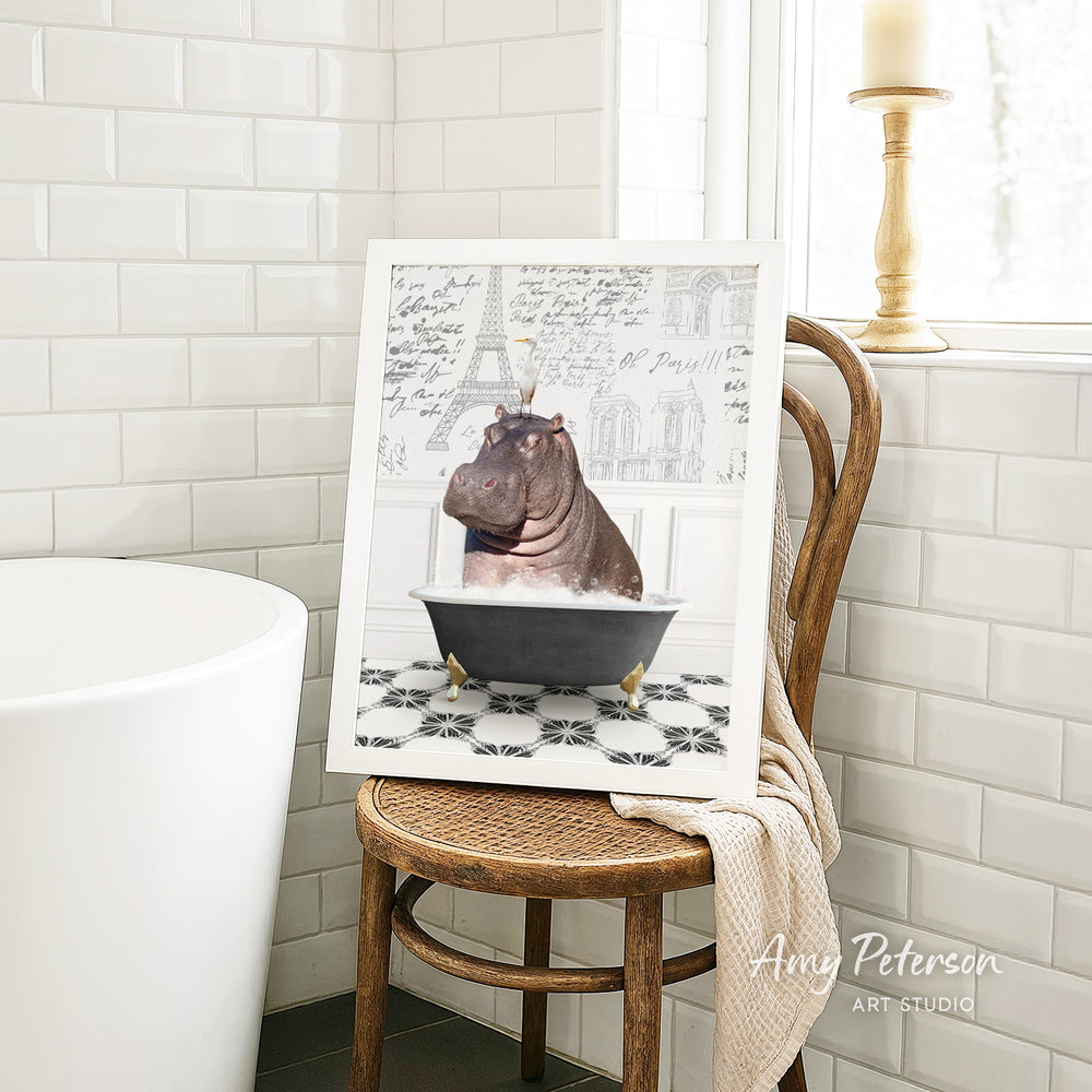 A framed image of a hippopotamus sitting in a bathtub, surrounded by a tiled pattern, is displayed on a wooden chair in a bathroom setting.