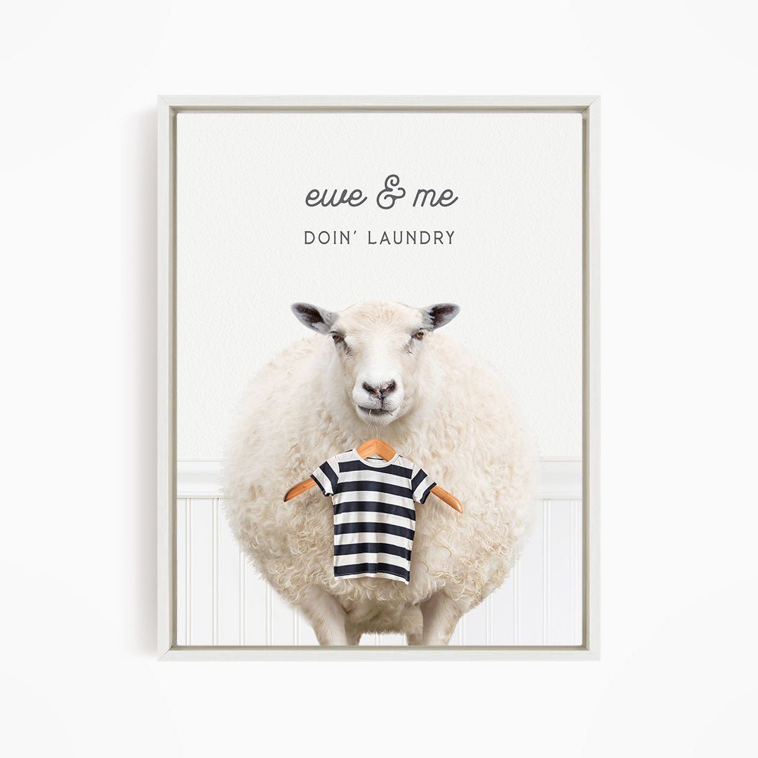 A white sheep standing in front of a white wall, with a striped shirt hanging from its neck.