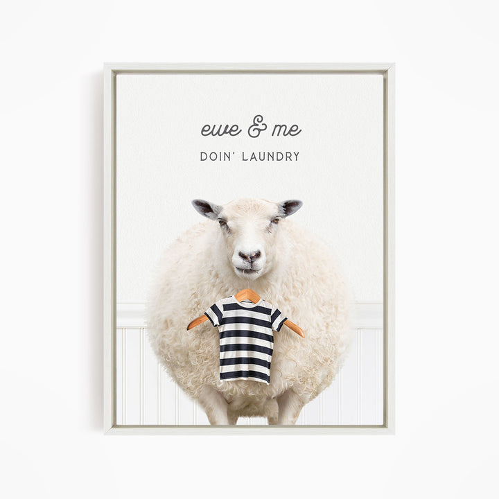 A white sheep standing in front of a white wall, with a striped shirt hanging from its neck.