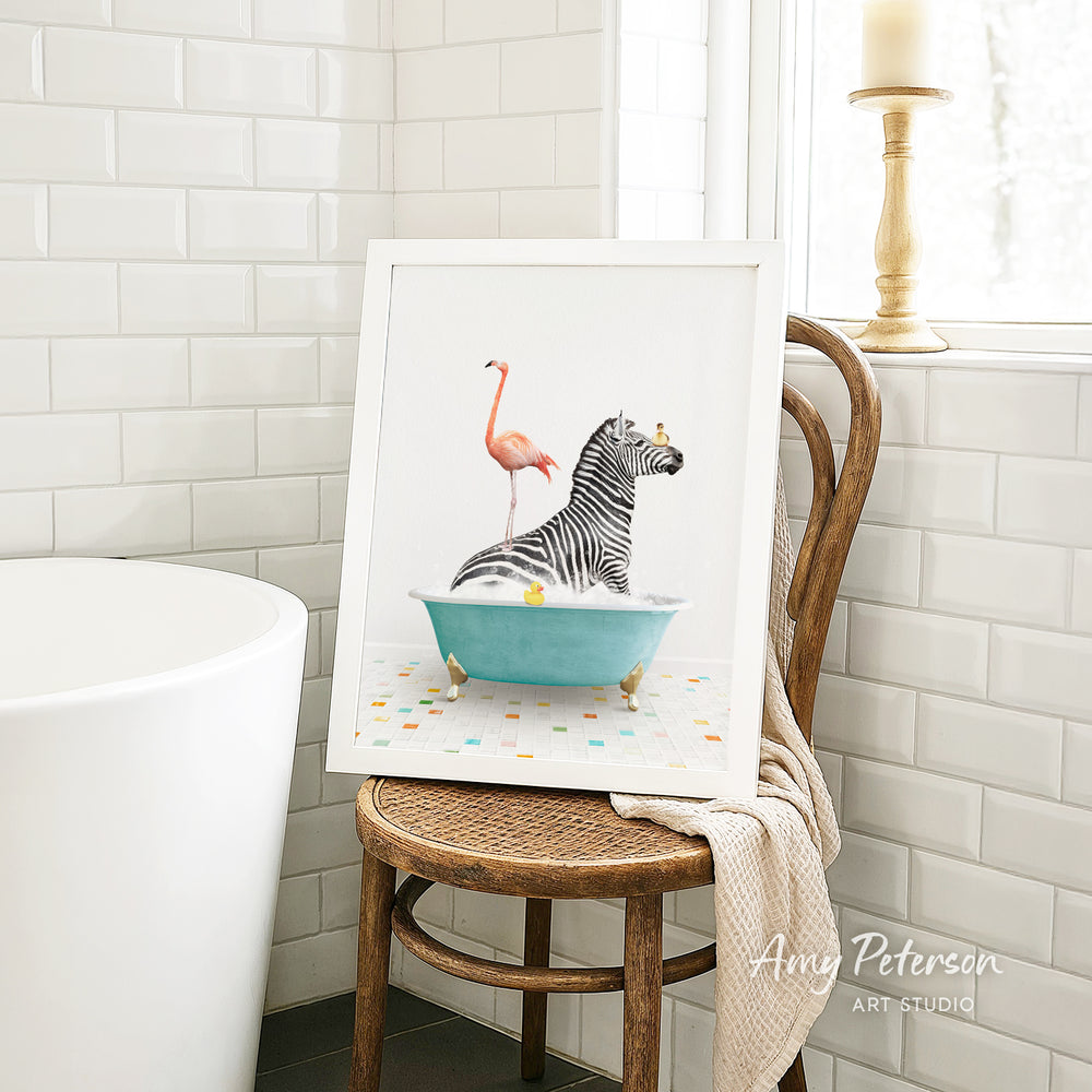 A framed illustration of a zebra sitting in a bathtub, with a pink flamingo standing on one leg next to it. The image is displayed on a wooden chair in a bathroom setting.