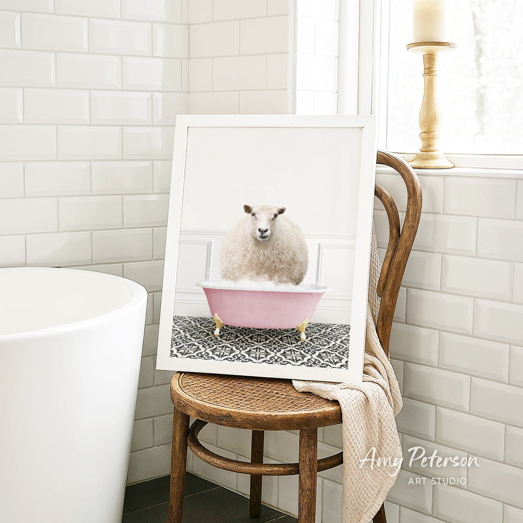 A framed image of a sheep sitting in a pink bathtub is displayed on a wooden chair in a bathroom setting.