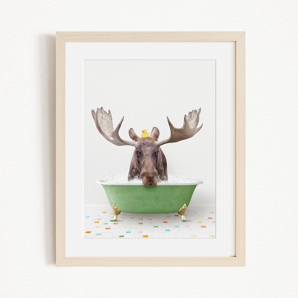 A moose with large antlers is sitting in a green bathtub, surrounded by colorful tiles on the floor.