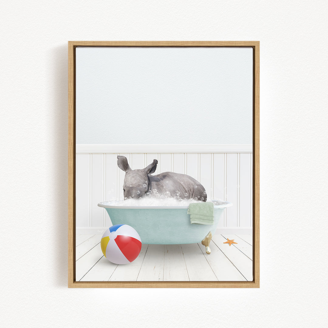 A gray rhinoceros is sitting in a blue bathtub filled with water, surrounded by a beach ball and a towel.
