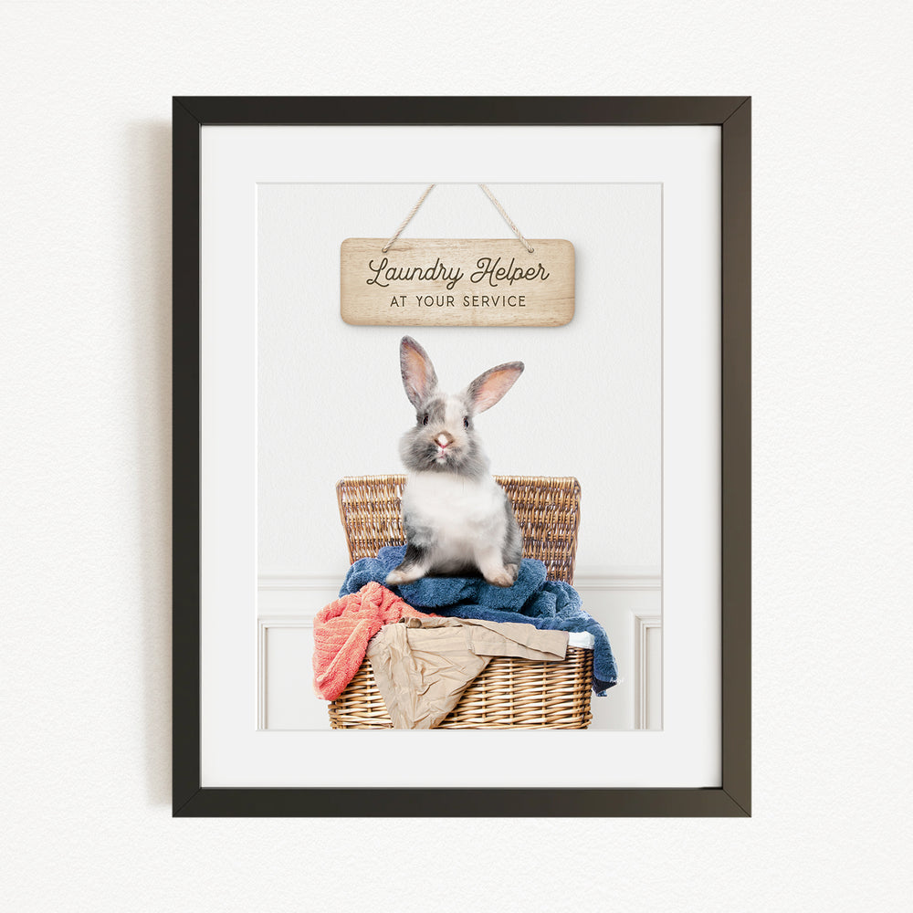 A framed image of a rabbit sitting in a wicker laundry basket, with a sign above that reads "Laundry Helper at your service".