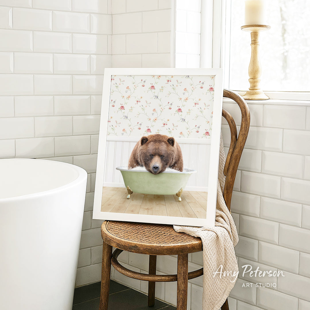 A framed image of a brown bear sitting in a green bathtub, with a floral pattern on the wall behind it.
