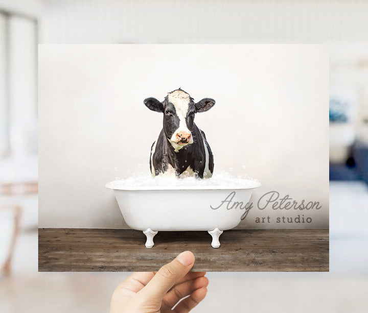 a hand holding up a card with a picture of a cow in a bathtub