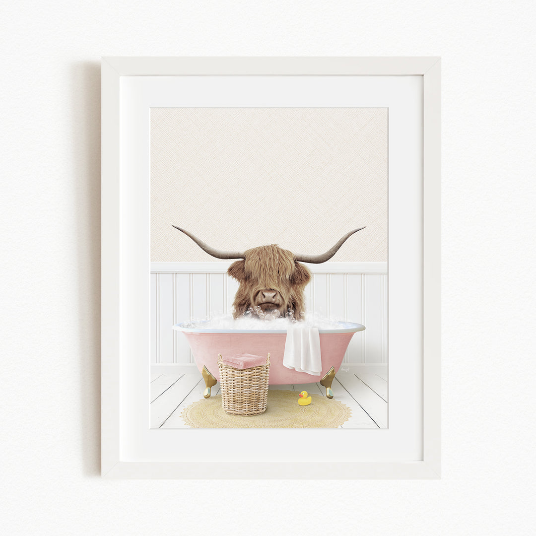 A brown cow with long horns is sitting in a pink bathtub, surrounded by a yellow rubber duck and a basket.