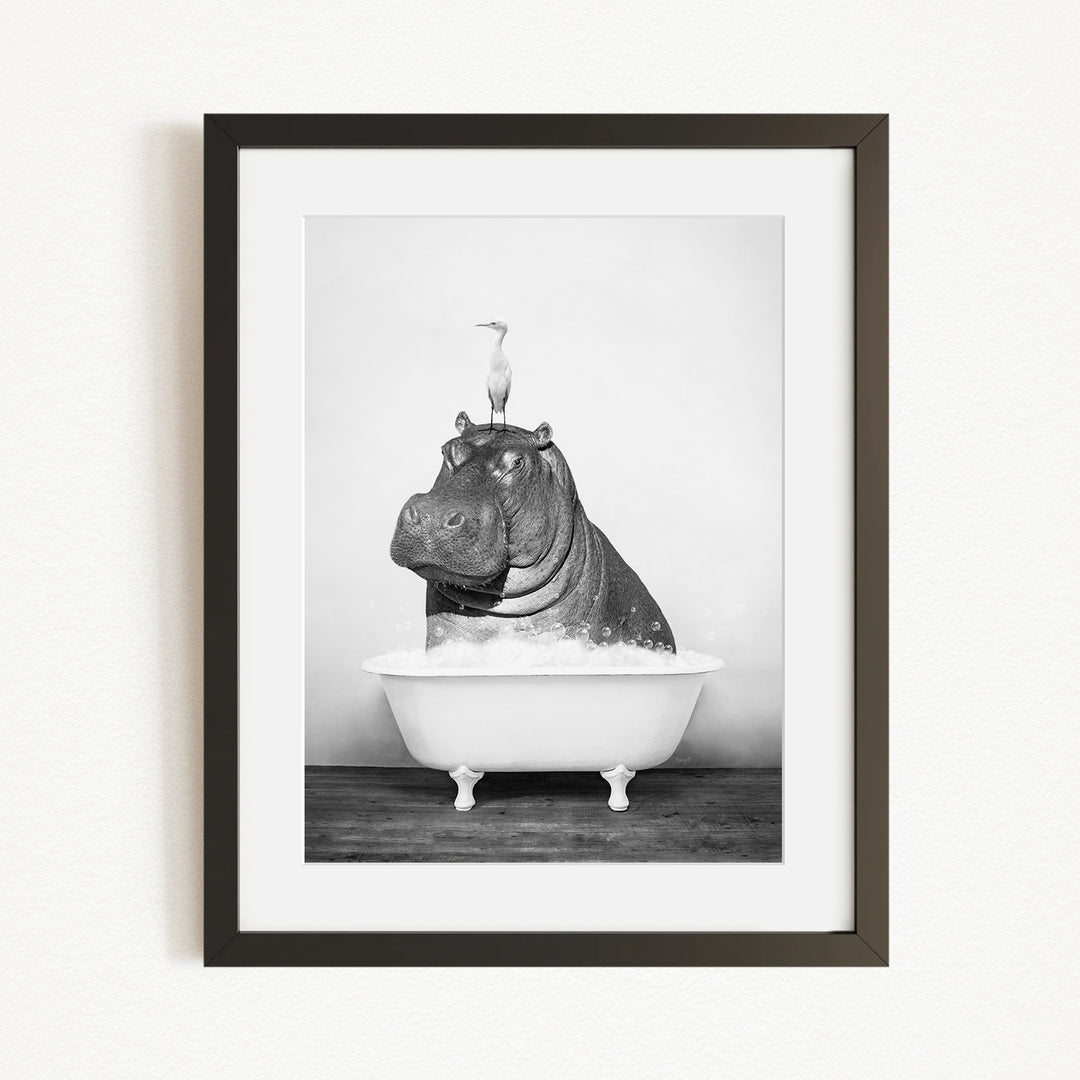 A black and white photograph of a hippopotamus sitting in a bathtub, with a bird perched on its head.