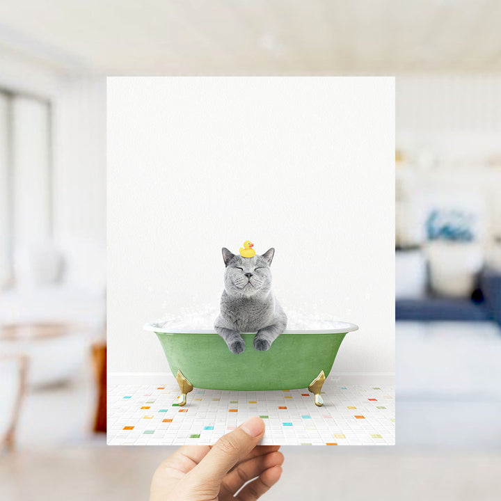 A gray cat sitting in a green bathtub, with a yellow rubber duck on its head, and a colorful tiled floor in the background.