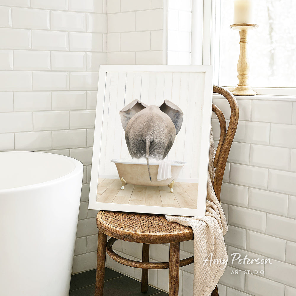 A framed image of an elephant sitting in a bathtub, with a towel draped over the back of the chair.