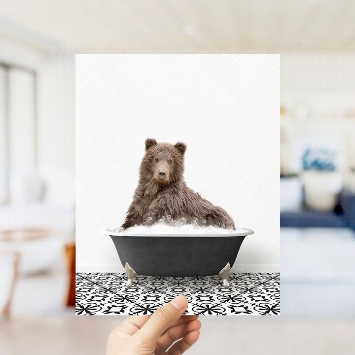 A brown bear sitting in a bathtub filled with bubbles, with a hand holding the image up to the camera.