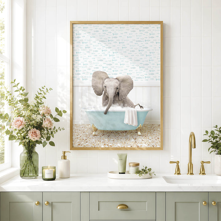A framed image of an elephant sitting in a bathtub, surrounded by flowers and a green vase, is displayed on a white tiled wall above a bathroom sink.