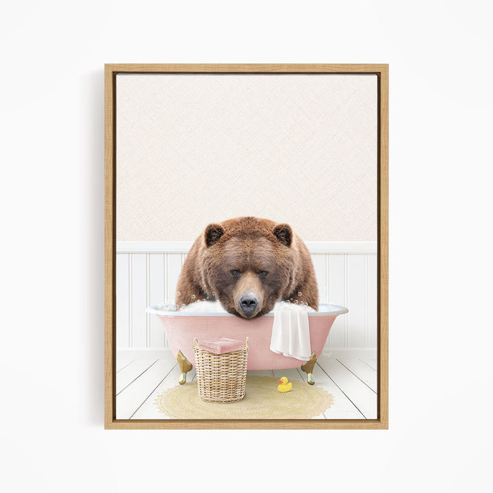 A brown bear is sitting in a pink bathtub filled with water, surrounded by a yellow rubber duck and a white towel.