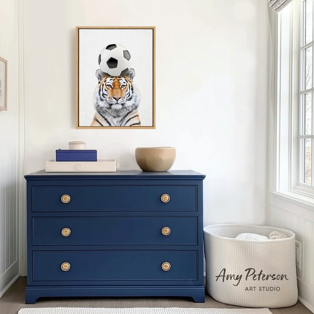 a tiger standing on a soccer ball, with a blue dresser and a basket in the foreground.