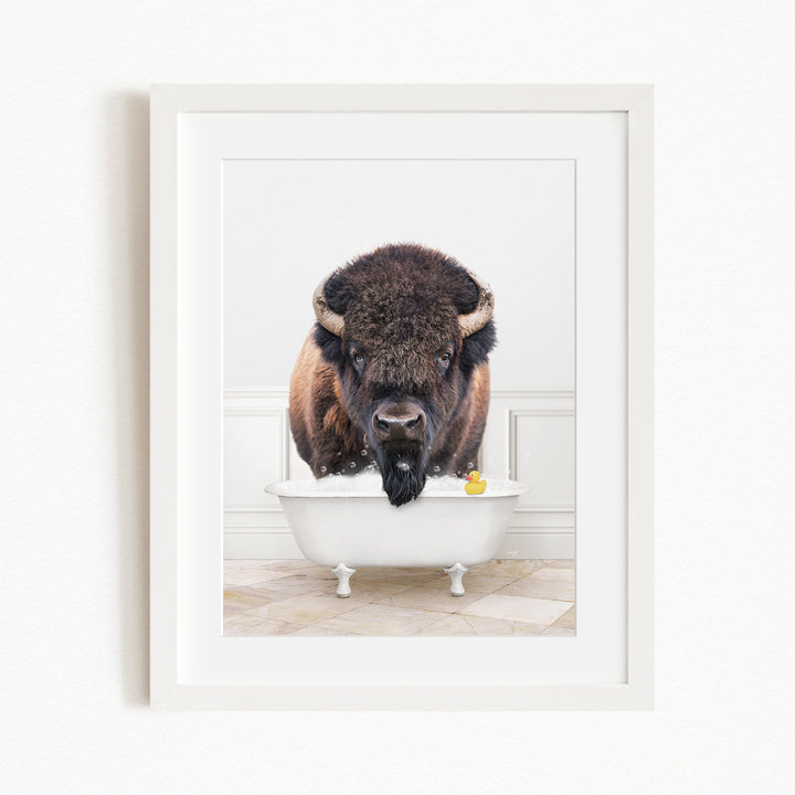 A buffalo with large horns is standing in a white bathtub, with a yellow rubber duck floating in the water.
