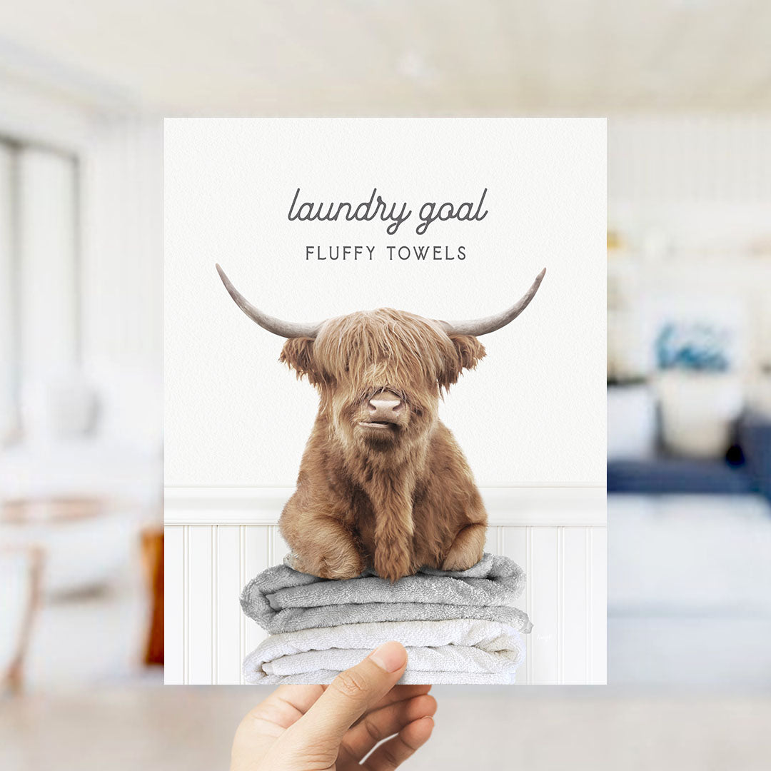 A hand holding up a poster with a large image of a horned animal, likely a yak or a yak dog, sitting on top of a stack of towels.