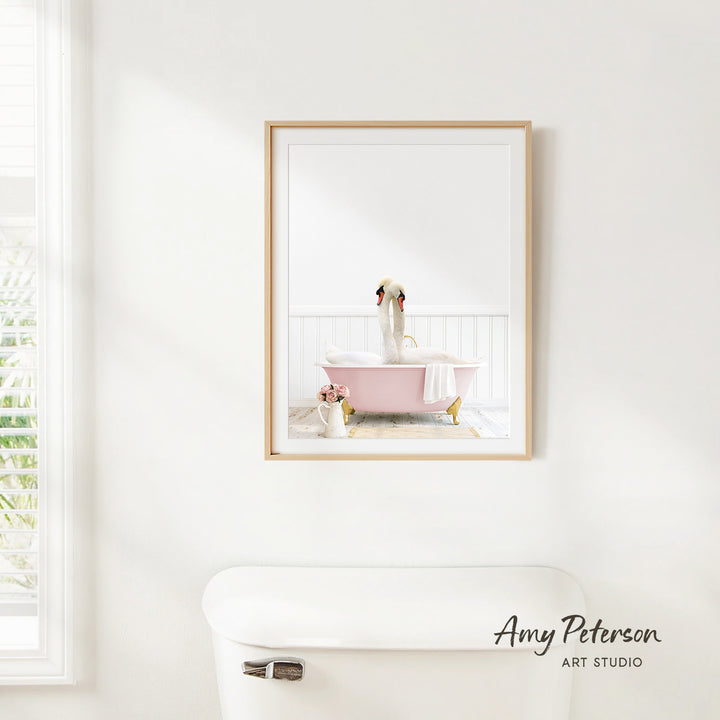 A framed image of a dog sitting in a pink bathtub is hanging on a white wall in a bathroom.